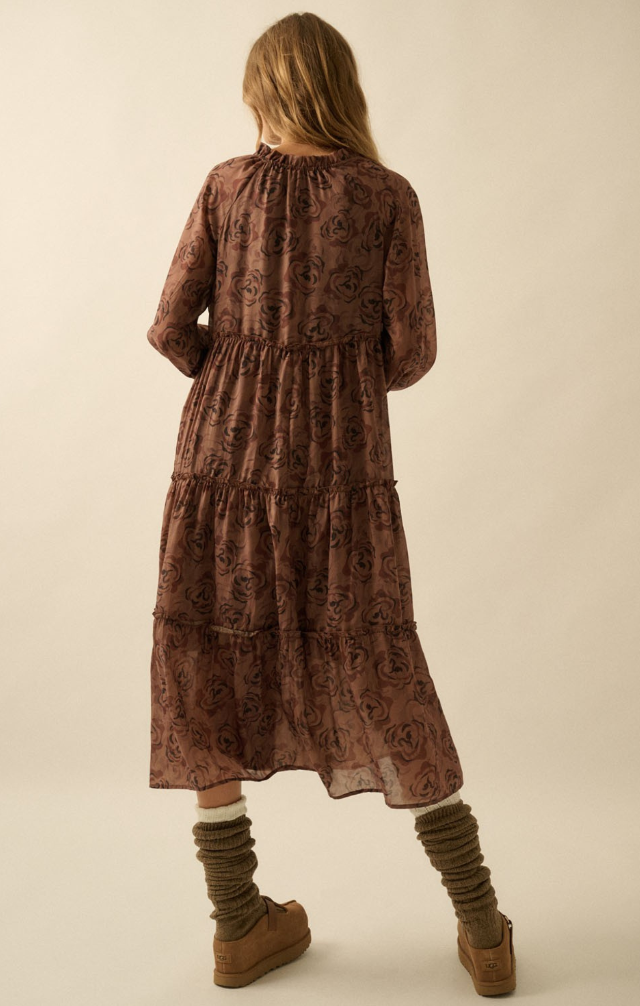 Woman wearing a brown patterned dress with long sleeves and layered skirt on a beige background