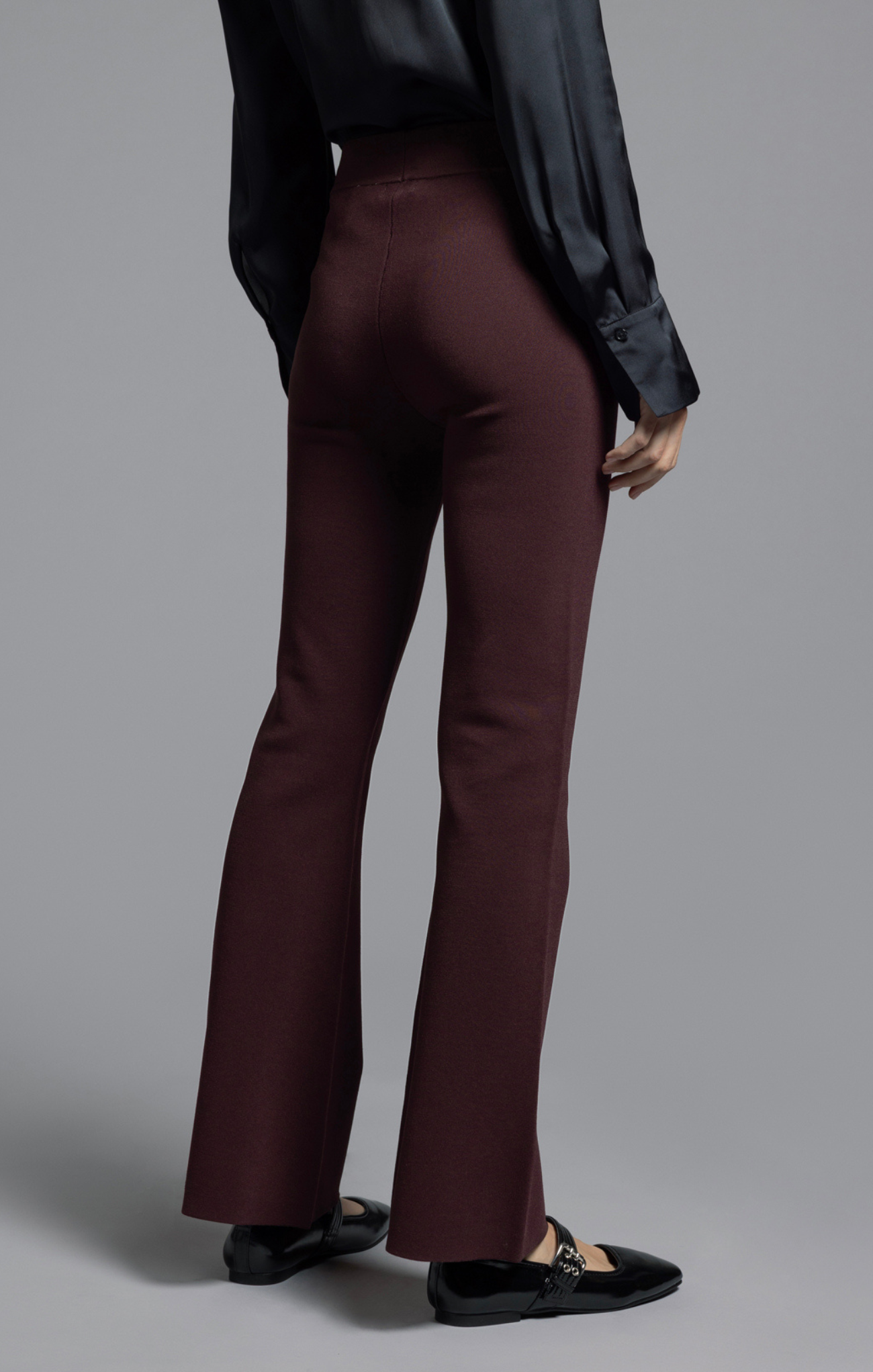 Person wearing maroon flared pants and a black top on a gray background