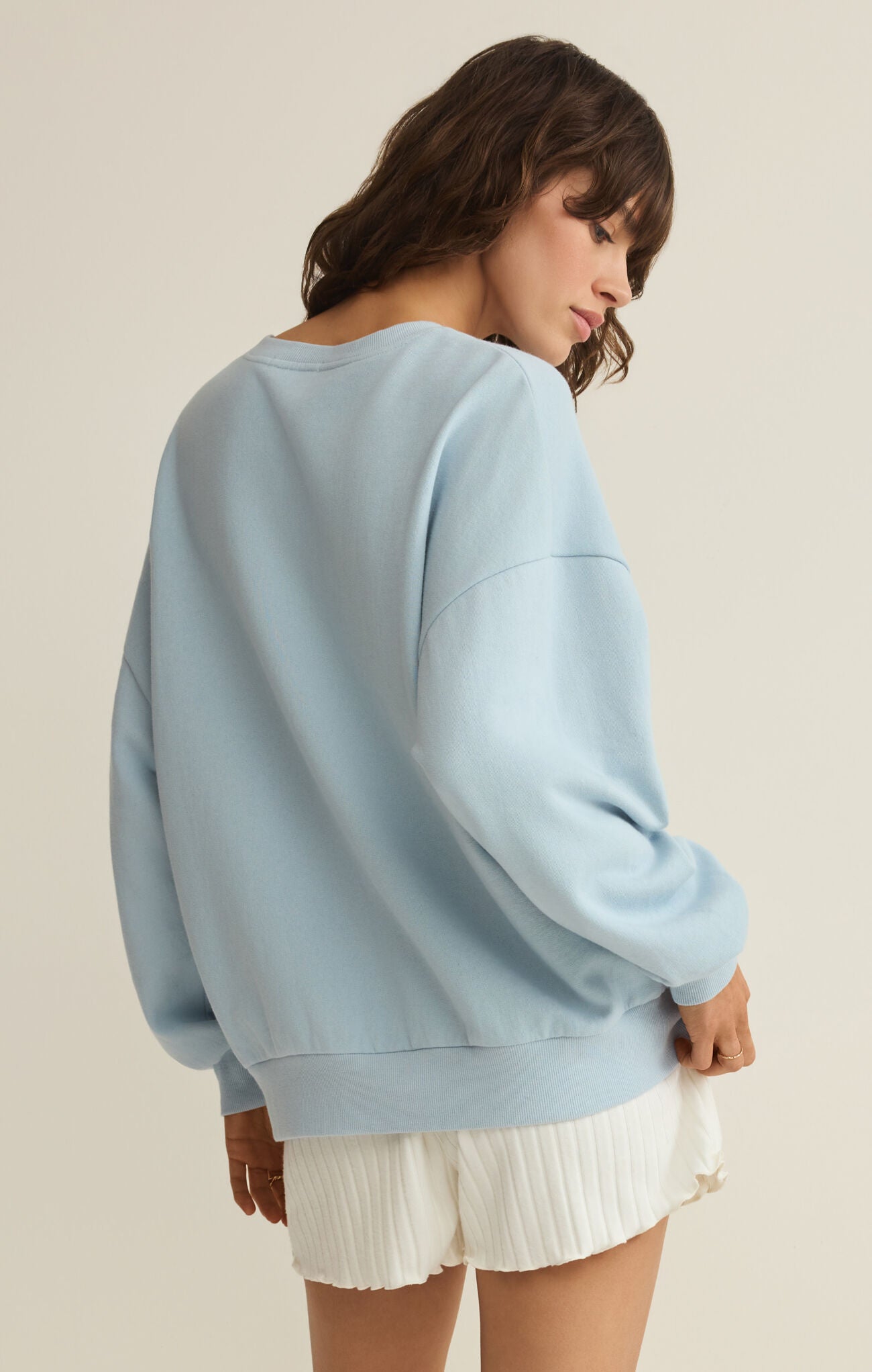 Woman wearing a light blue sweatshirt and white shorts on a beige background