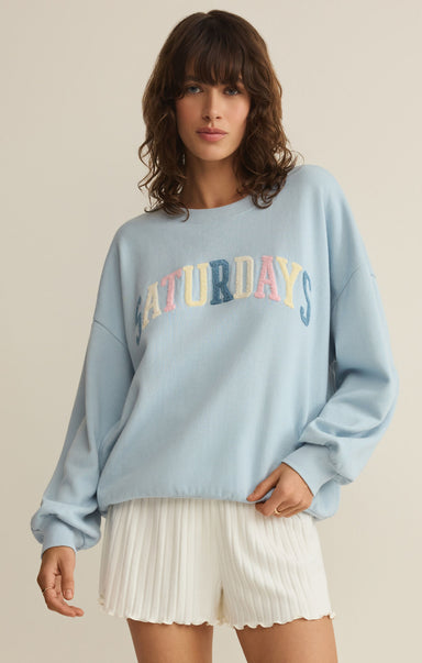 Woman wearing a light blue sweatshirt with 'Saturdays' text, standing against a plain background