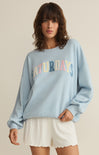 Woman wearing a light blue sweatshirt with 'Saturdays' text, standing against a plain background