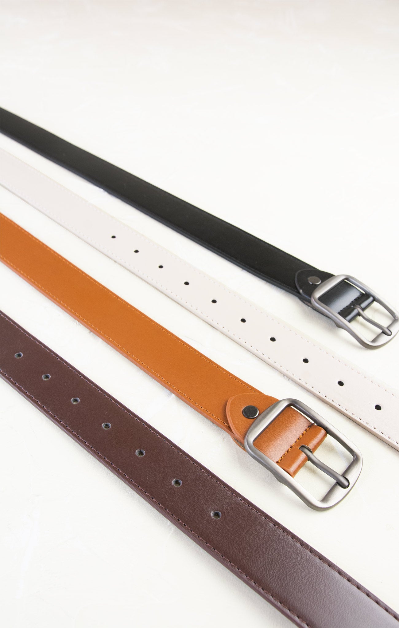 Three belts in black, brown, and white with silver buckles on a white background
