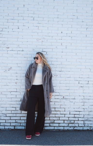 Person wearing a gray coat and sunglasses against a white brick wall