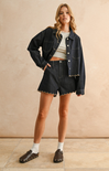 Woman wearing a denim jacket and shorts against a beige background