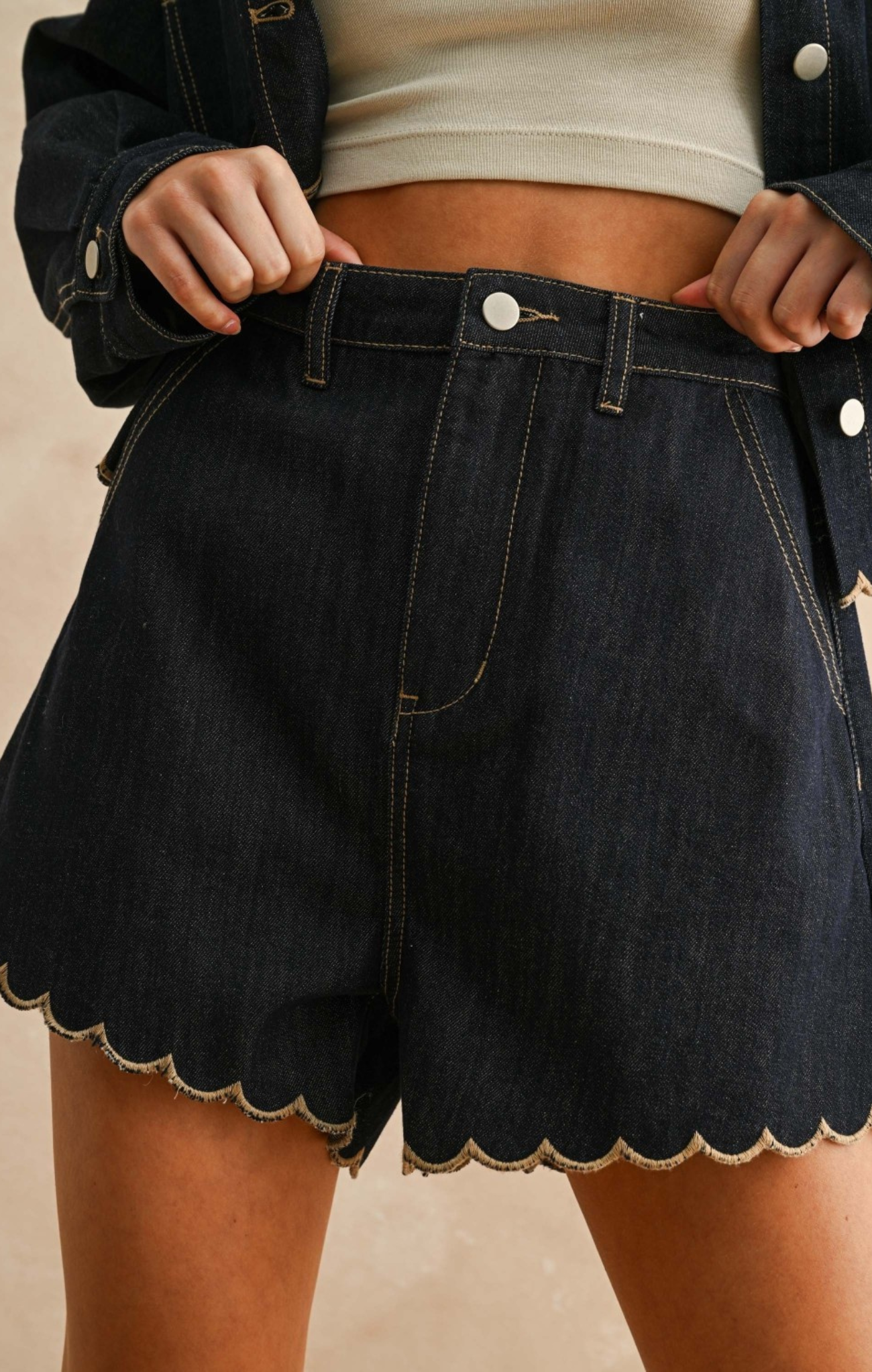 Person wearing black denim shorts with scalloped hem on a neutral background