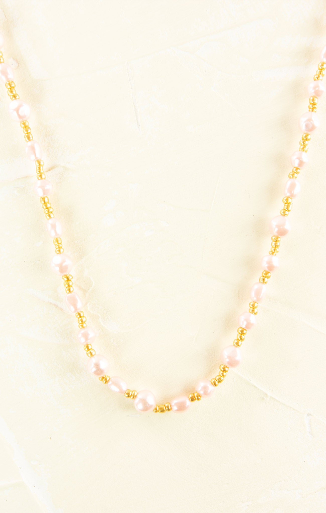 Necklace with pink beads and gold accents on a light yellow background