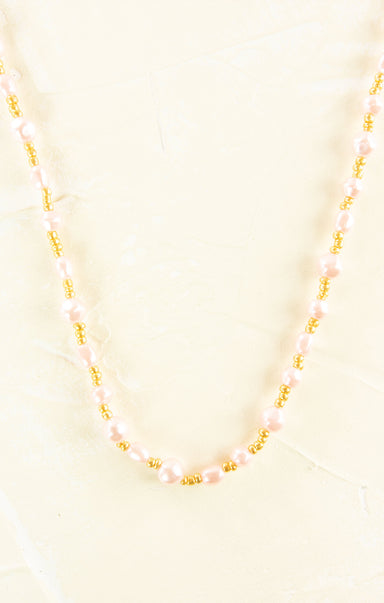 Necklace with pink beads and gold accents on a light yellow background