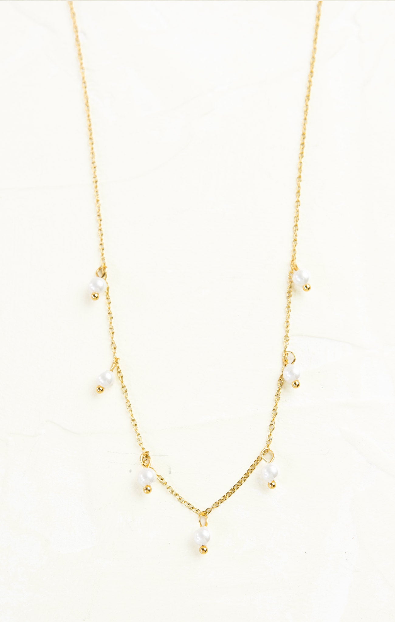 Gold necklace with small pearls on a white background
