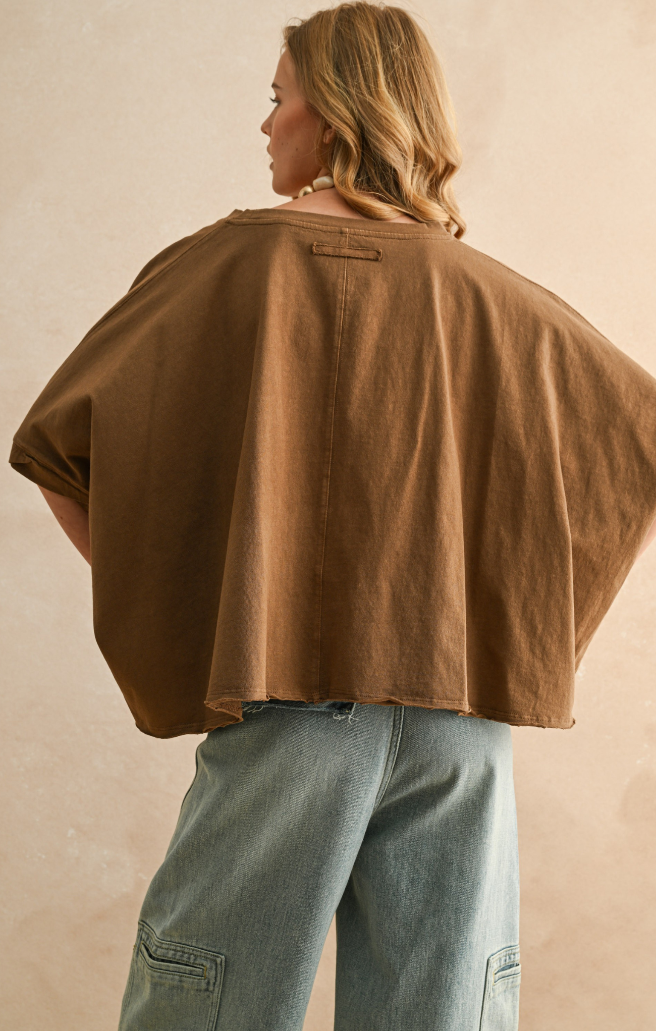 Person wearing a brown cape over a beige background