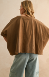 Person wearing a brown cape over a beige background