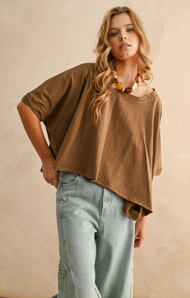 Woman wearing a brown oversized shirt and light blue jeans against a beige background