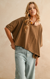 Woman wearing a brown oversized shirt and light blue jeans against a beige background