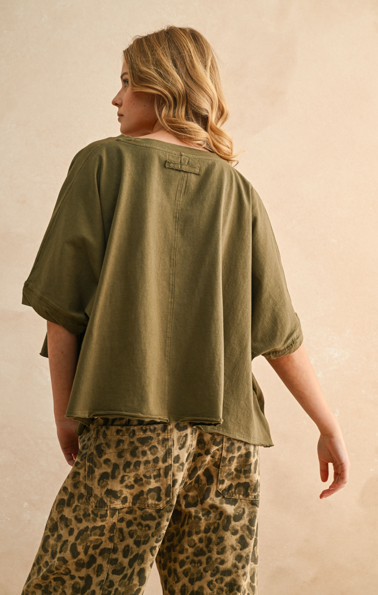 Person wearing an olive green shirt and leopard print pants against a beige background