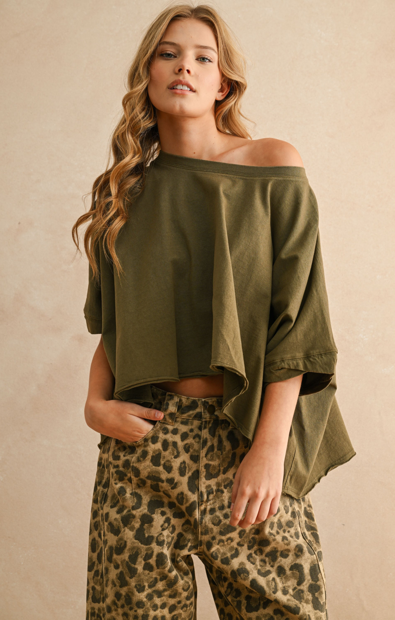 Woman wearing an olive green off-shoulder top and leopard print pants against a beige background