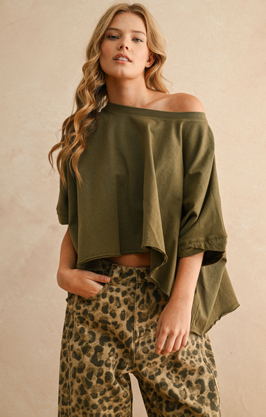 Woman wearing an olive green off-shoulder top and leopard print pants against a beige background