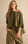 Woman wearing an olive green off-shoulder top and leopard print pants against a beige background