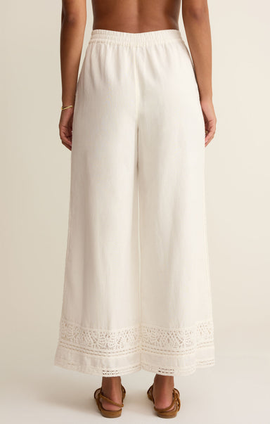 White wide-leg pants with lace trim worn by a person on a beige background