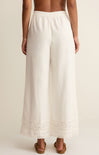 White wide-leg pants with lace trim worn by a person on a beige background