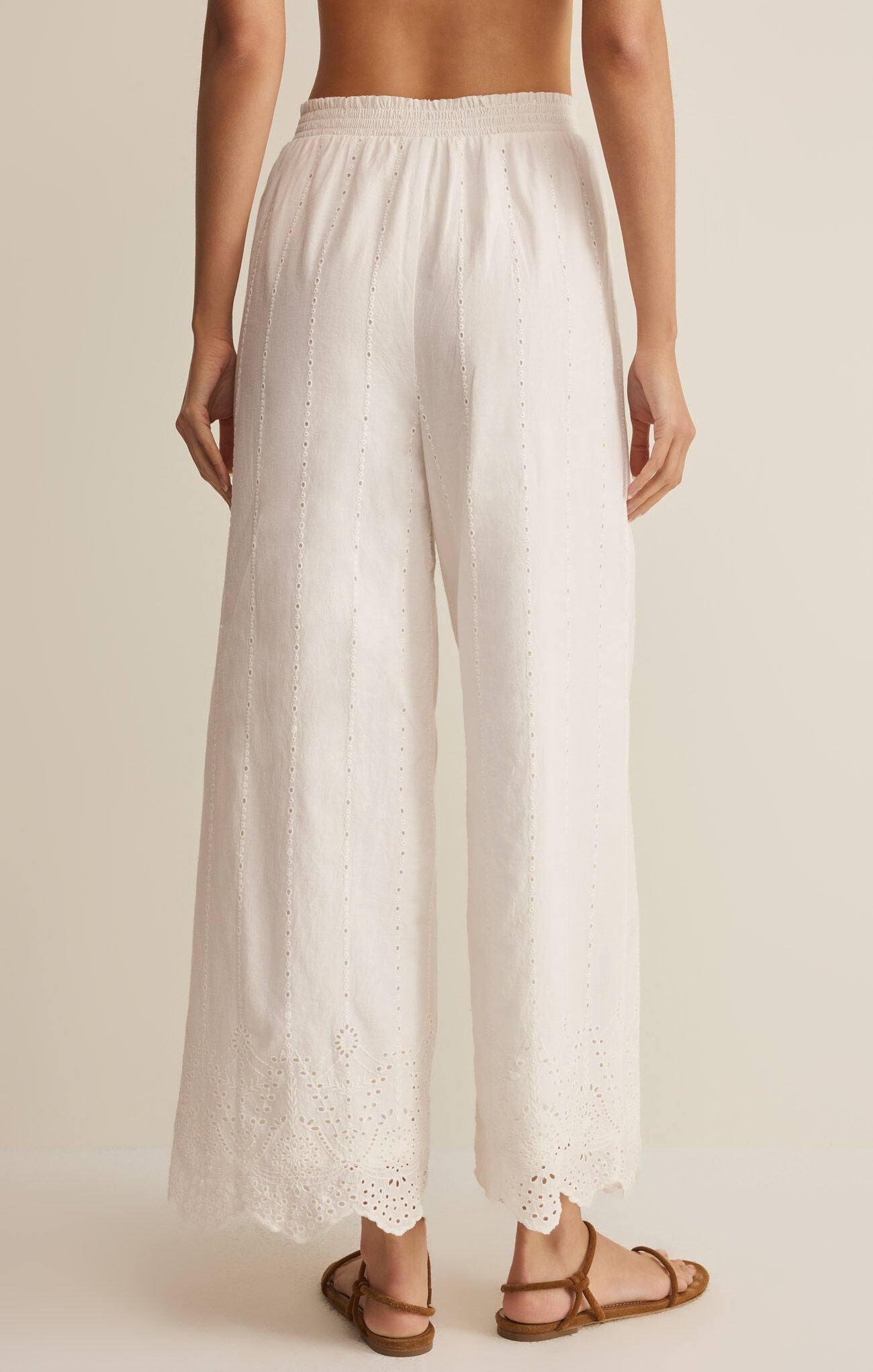 White wide-leg pants with lace trim worn by a person on a beige background