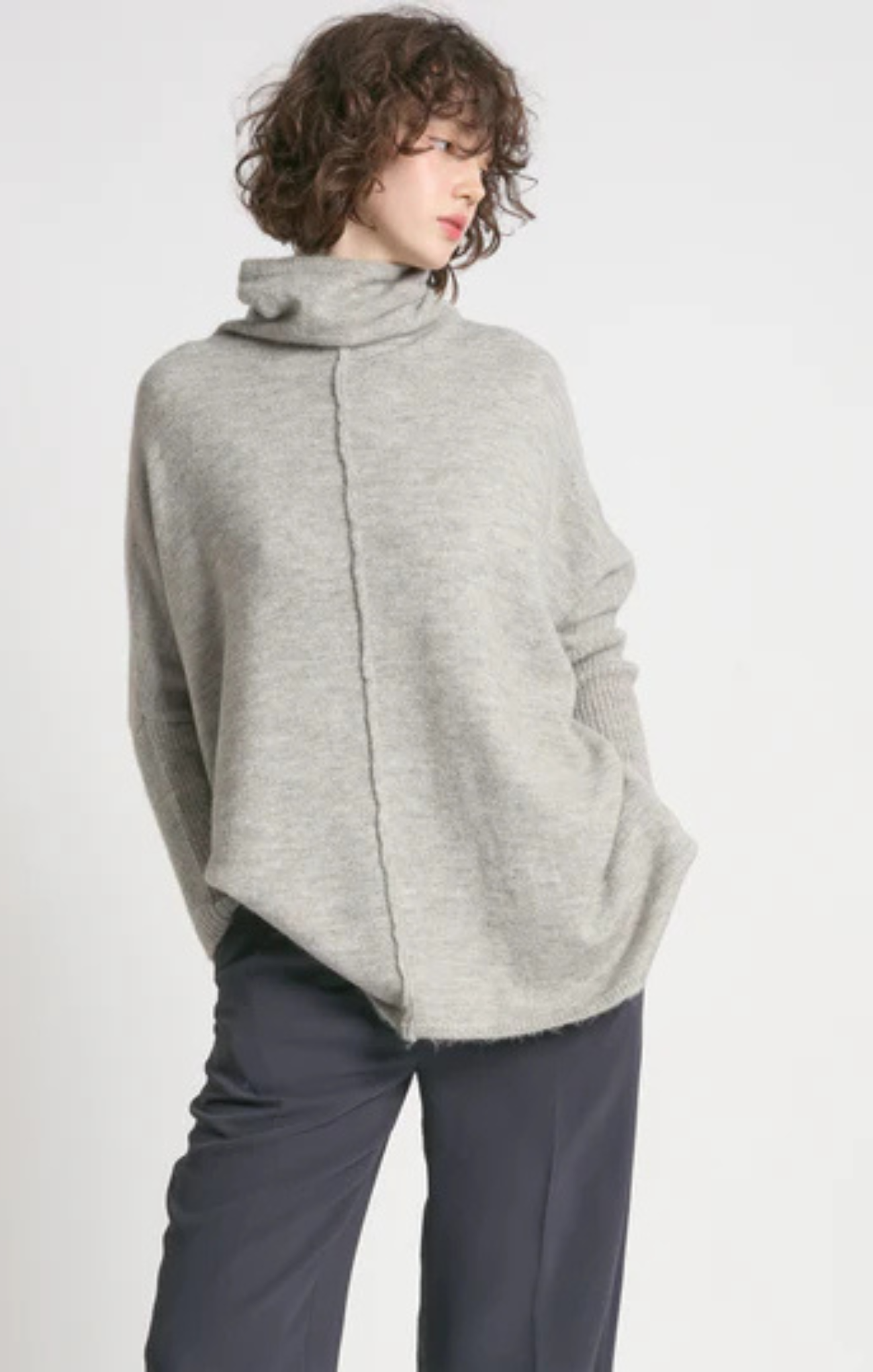 Person wearing a gray poncho over a dark outfit on a white background