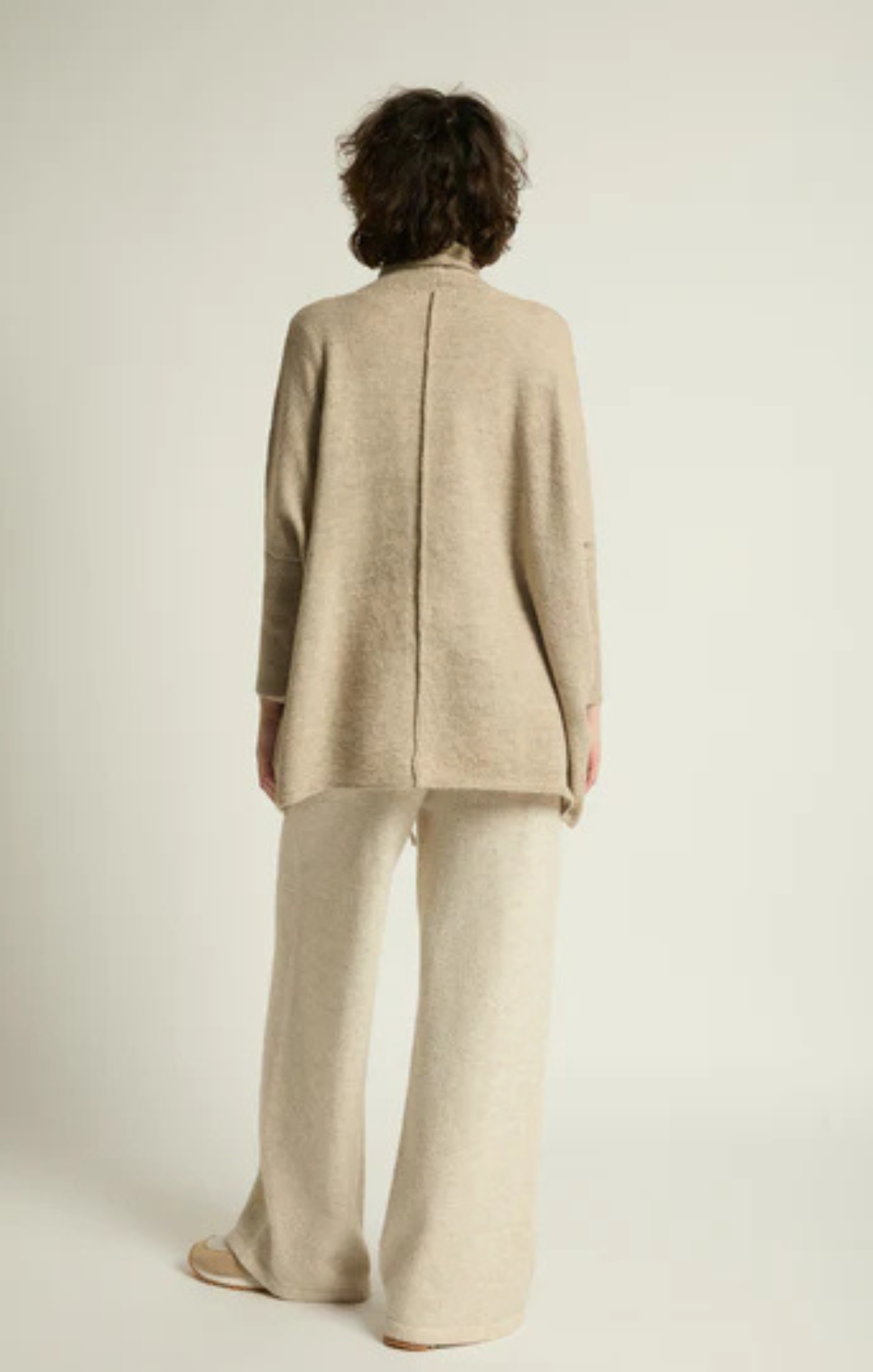 Person wearing a beige coat and pants on a plain background