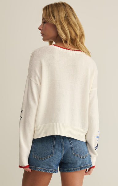 Woman wearing a white sweater with star designs and denim shorts on a plain background