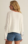Woman wearing a white sweater with star designs and denim shorts on a plain background