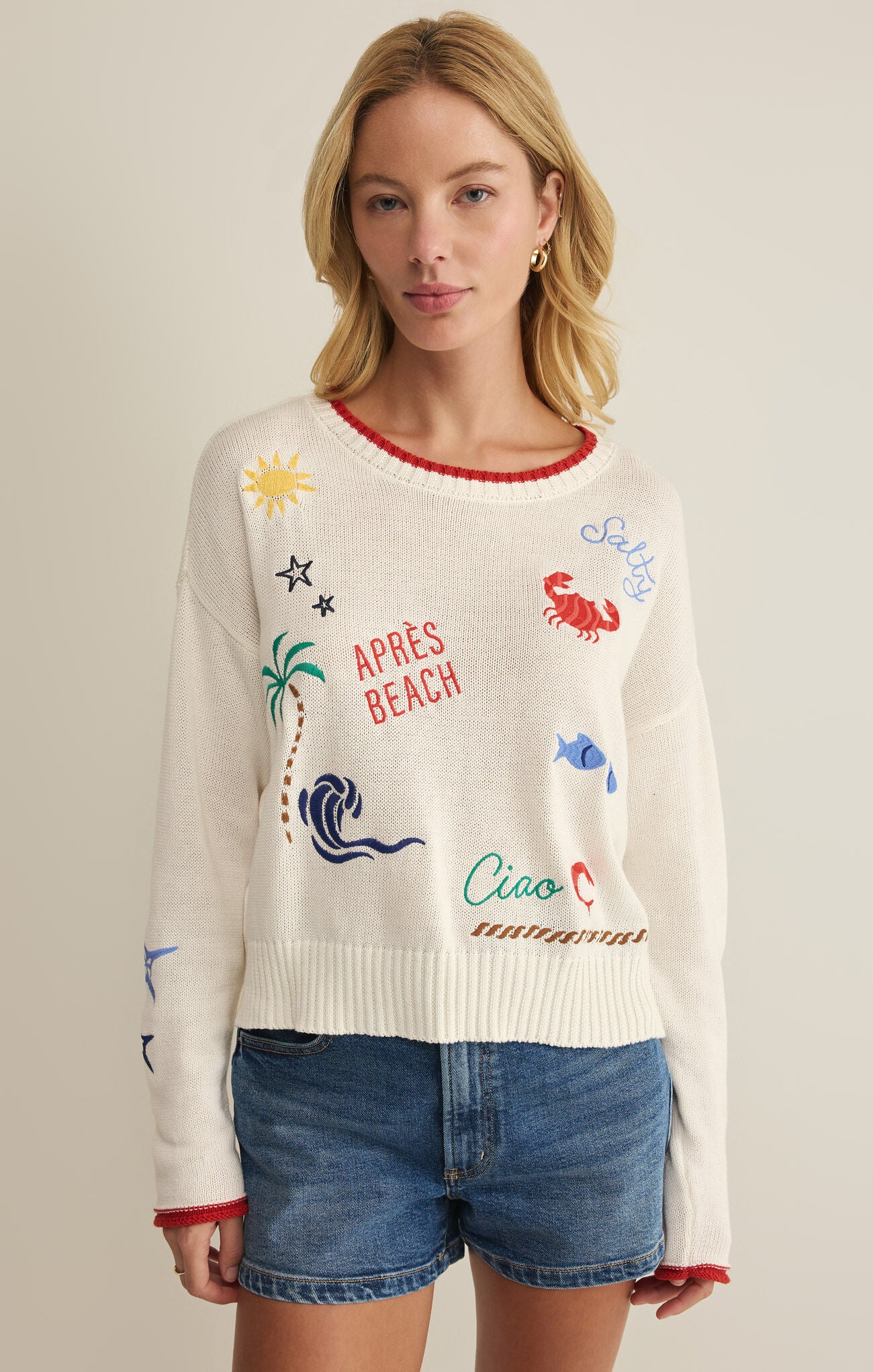Woman wearing a cream sweater with colorful graphics and text on a plain background