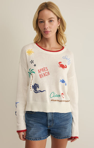 Woman wearing a cream sweater with colorful graphics and text on a plain background