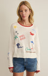 Woman wearing a cream sweater with colorful graphics and text on a plain background