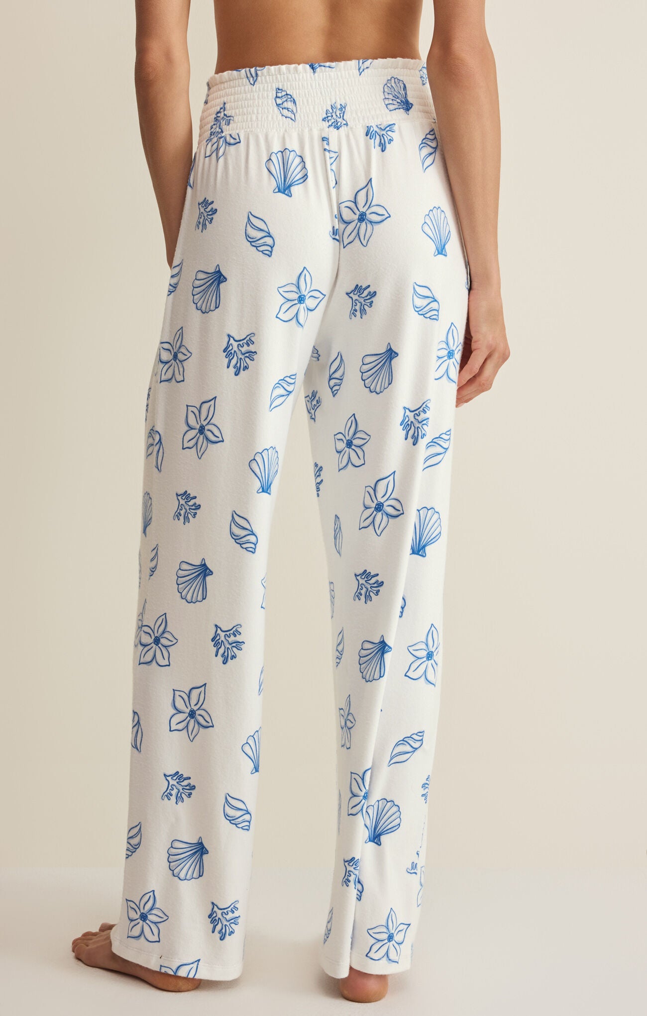 White pajama pants with blue floral pattern worn by a person on a neutral background