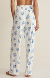 White pajama pants with blue floral pattern worn by a person on a neutral background