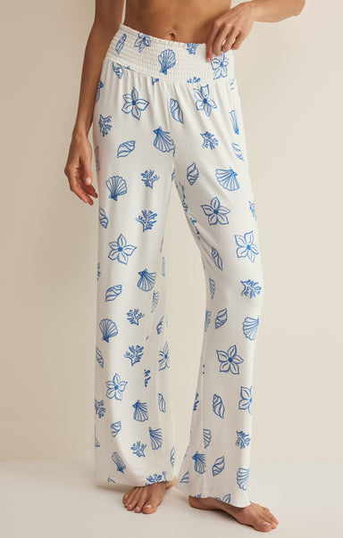 White pajama pants with blue floral patterns worn by a person on a beige background