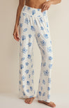 White pajama pants with blue floral patterns worn by a person on a beige background