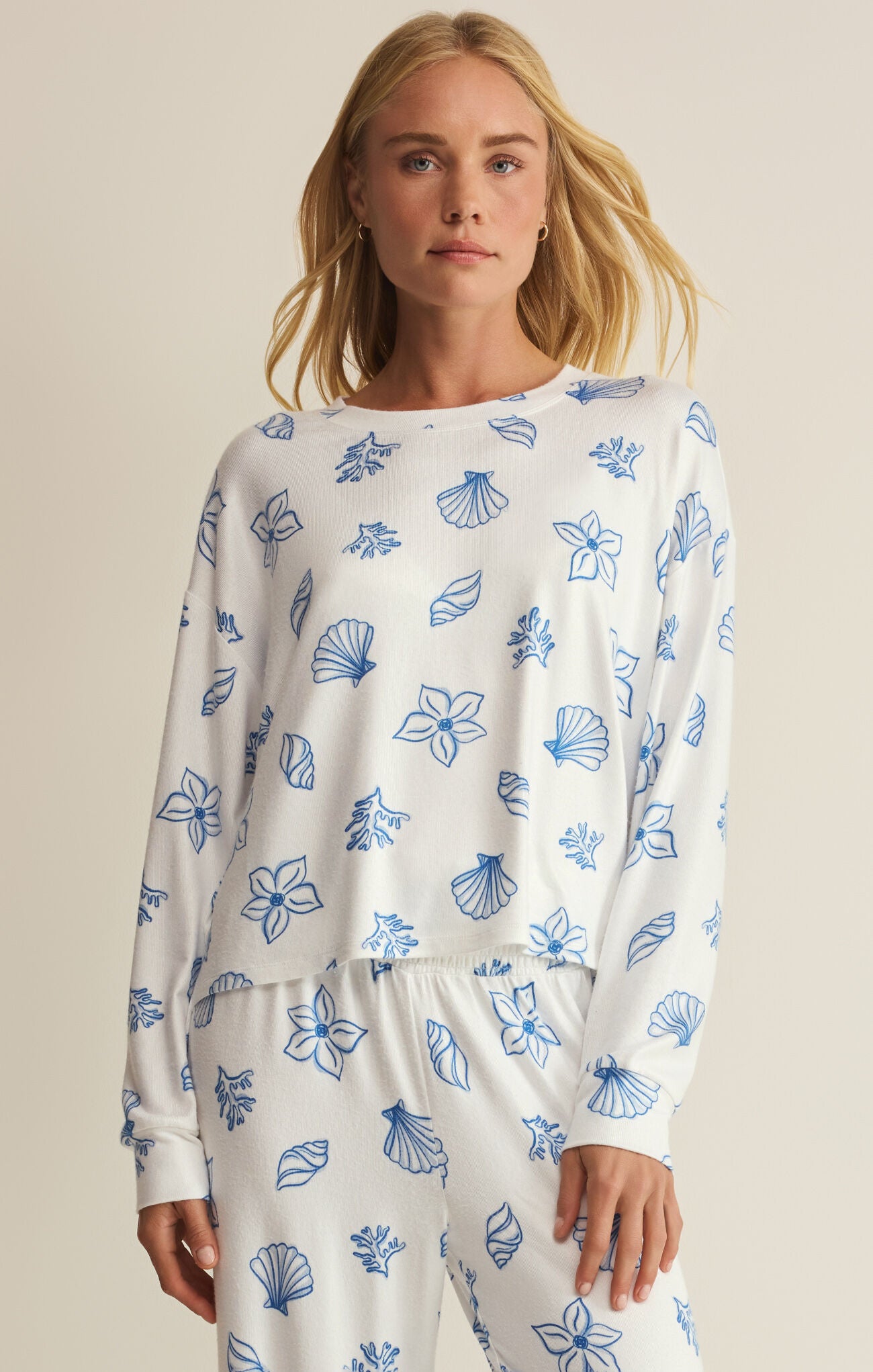Woman wearing a white long-sleeve top and pants with blue shell pattern on a beige background
