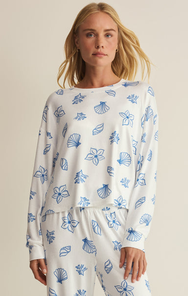 Woman wearing a white long-sleeve top and pants with blue shell pattern on a beige background