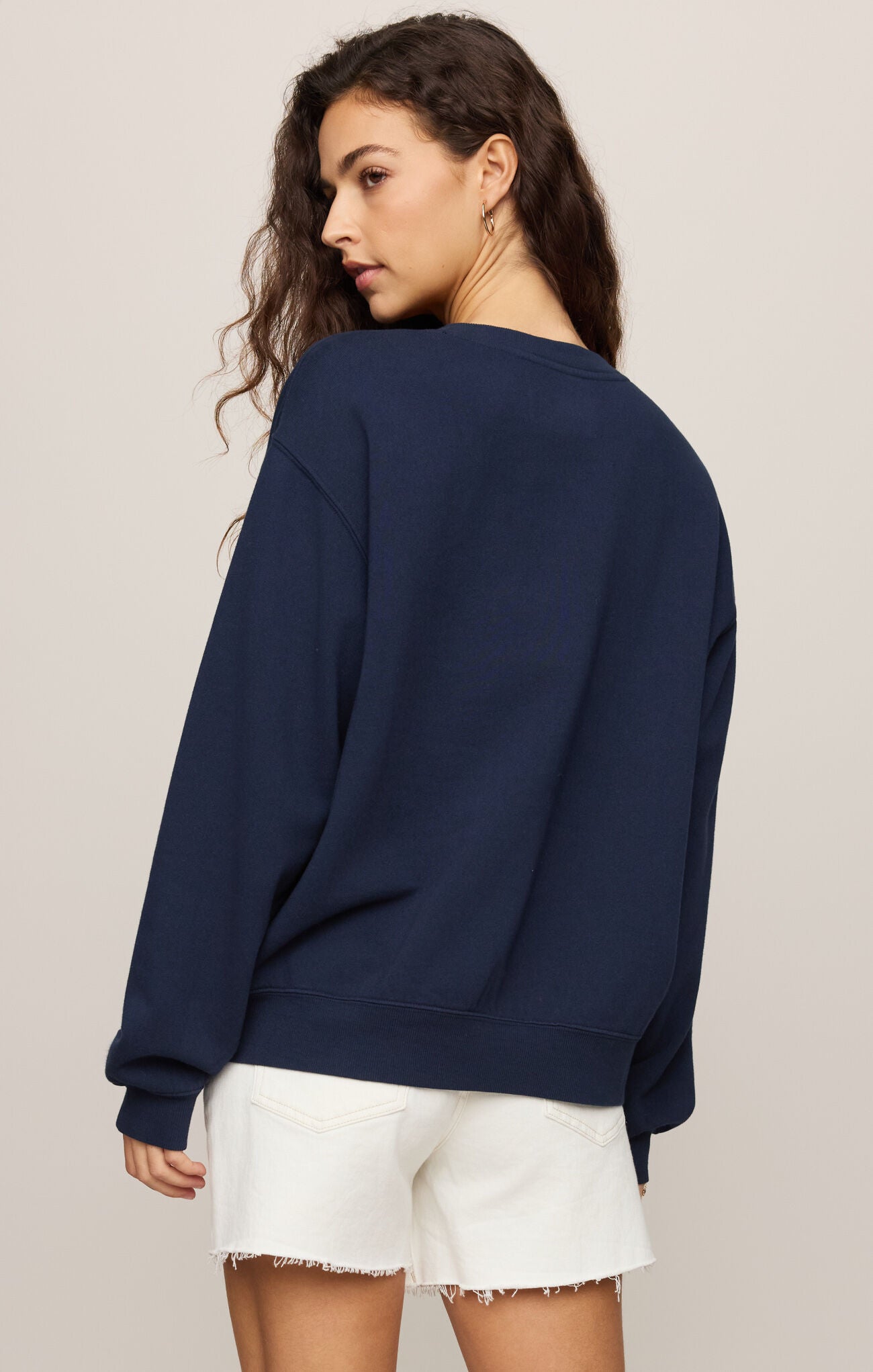 Woman wearing a navy blue sweatshirt and white shorts on a beige background