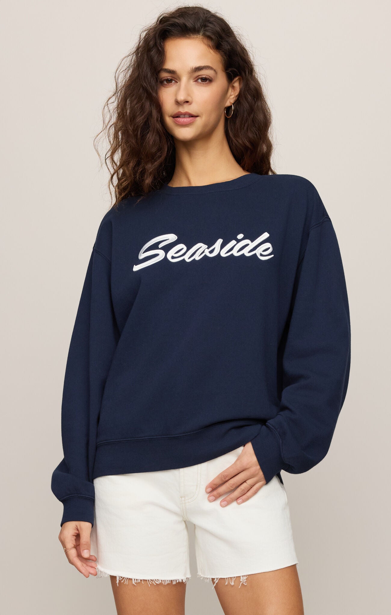Woman wearing a navy blue sweatshirt with 'Seaside' text on a beige background