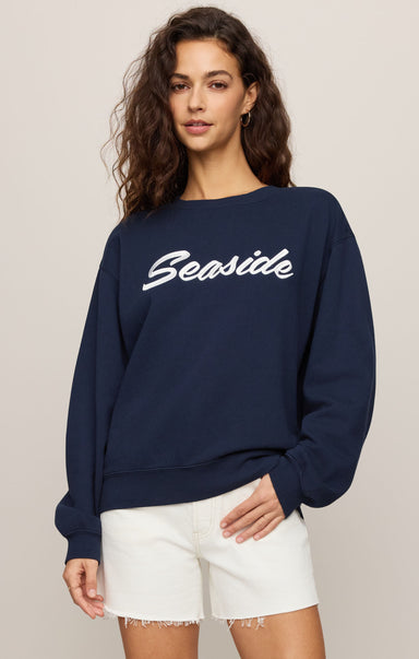 Woman wearing a navy blue sweatshirt with 'Seaside' text on a beige background