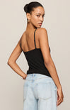 Woman wearing a black tank top and light blue jeans against a beige background