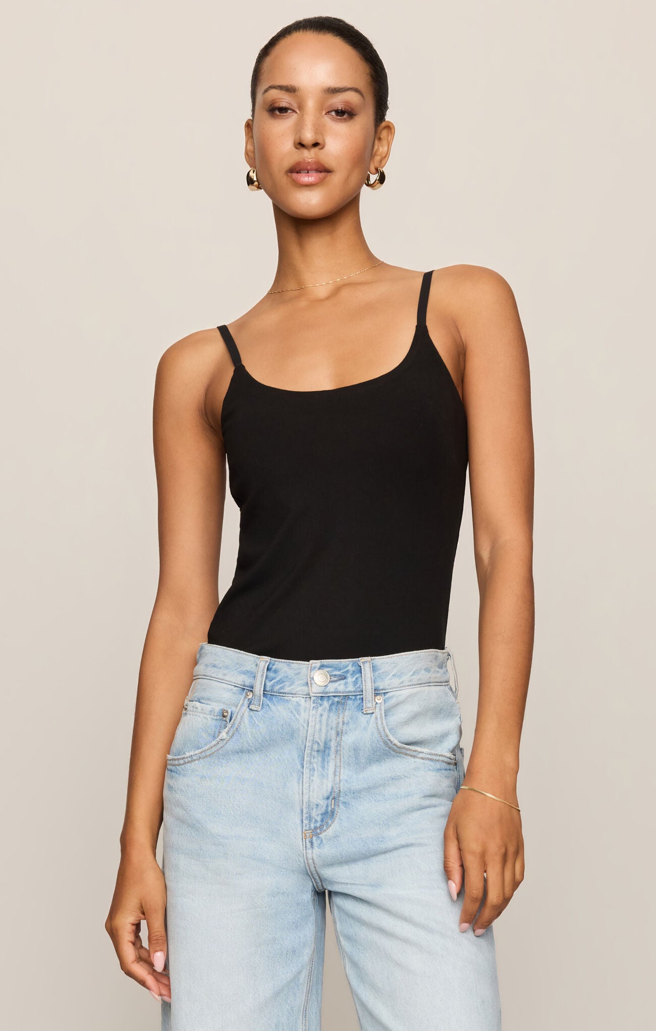 Woman wearing a black tank top and light blue jeans on a beige background