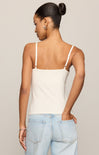 Woman wearing a beige tank top and light blue jeans against a neutral background