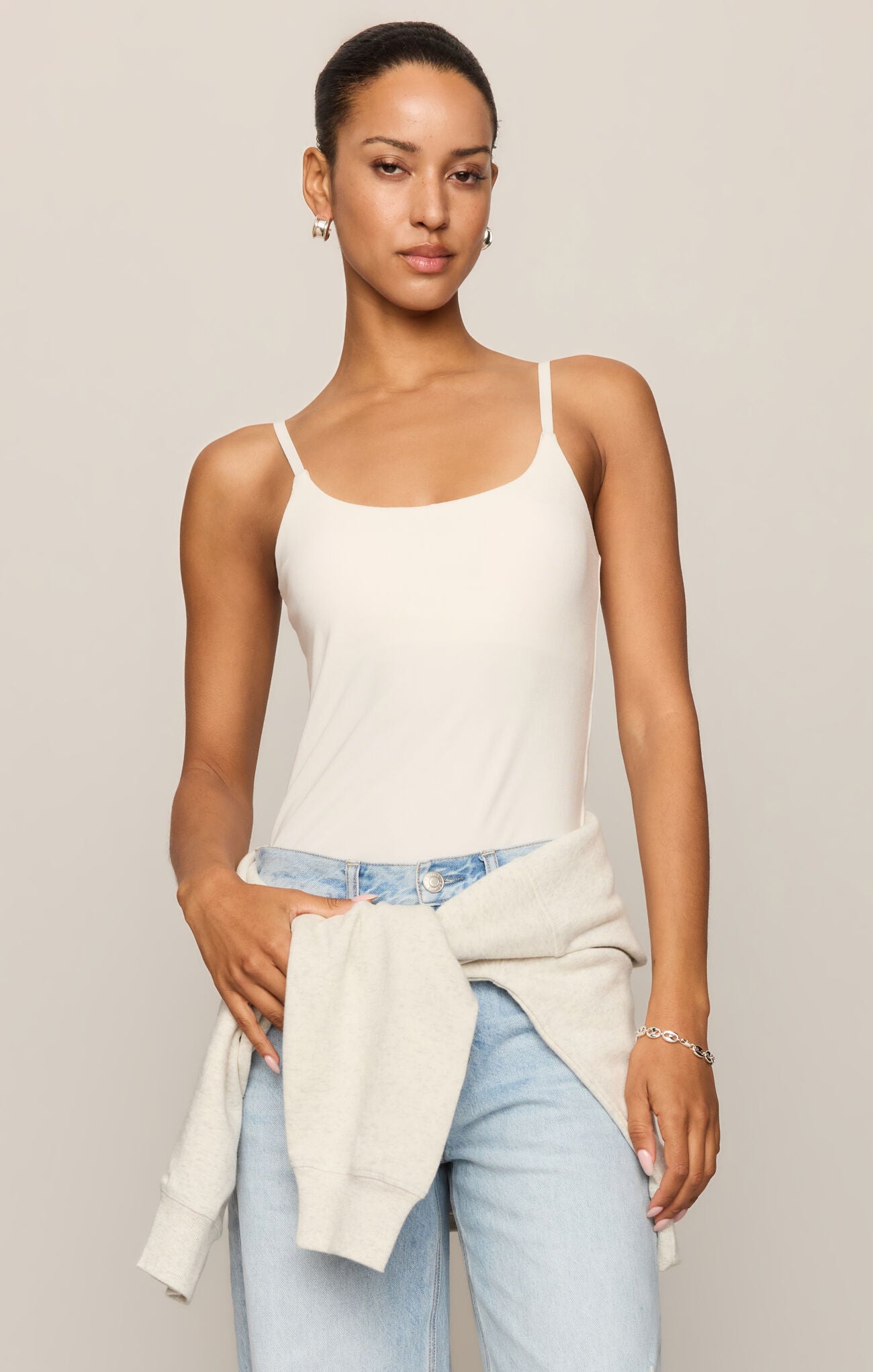 Woman wearing a white tank top and light blue jeans against a plain background