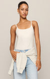 Woman wearing a white tank top and light blue jeans against a plain background