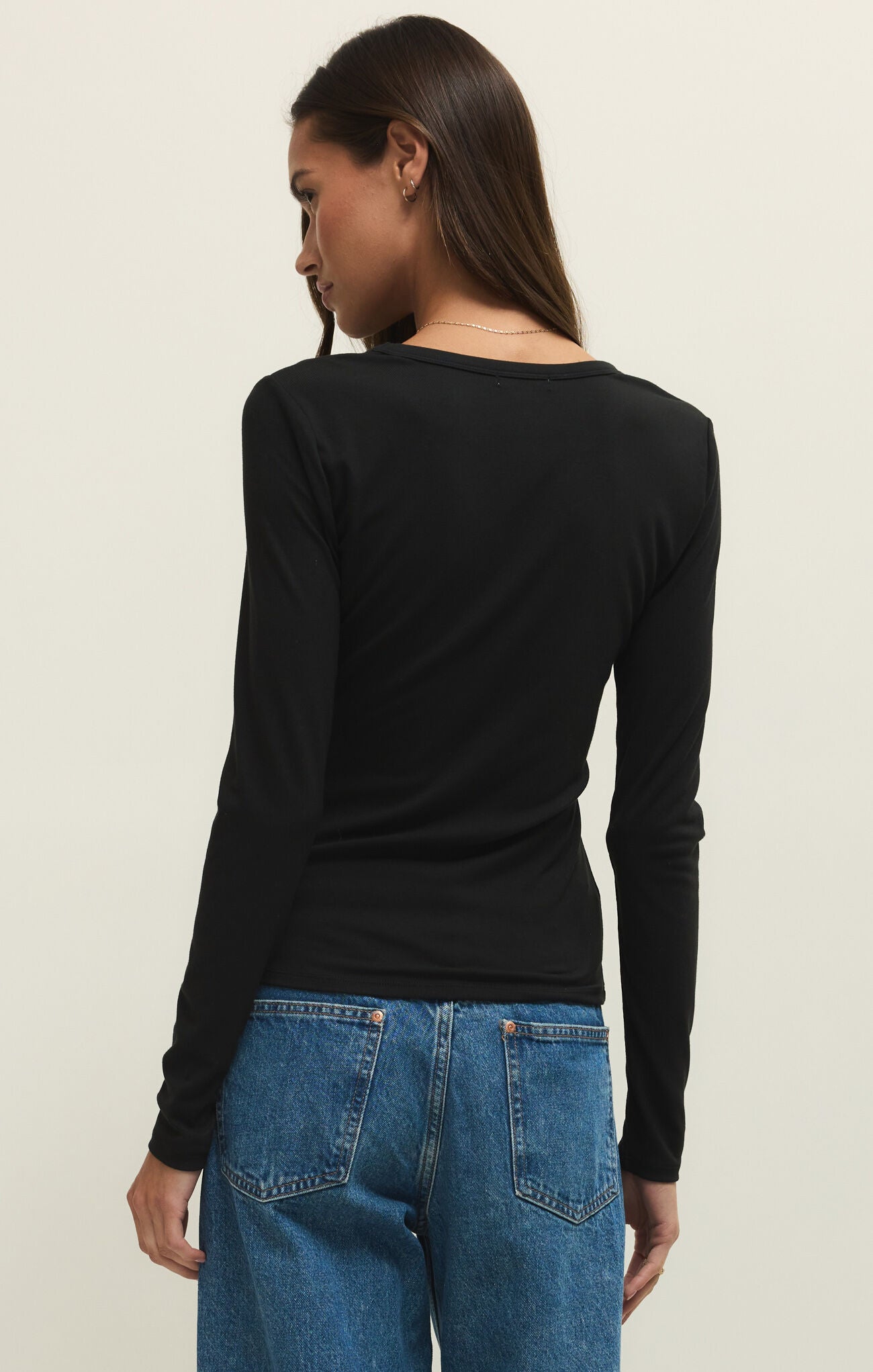 Person wearing a black long-sleeve top and blue jeans on a beige background