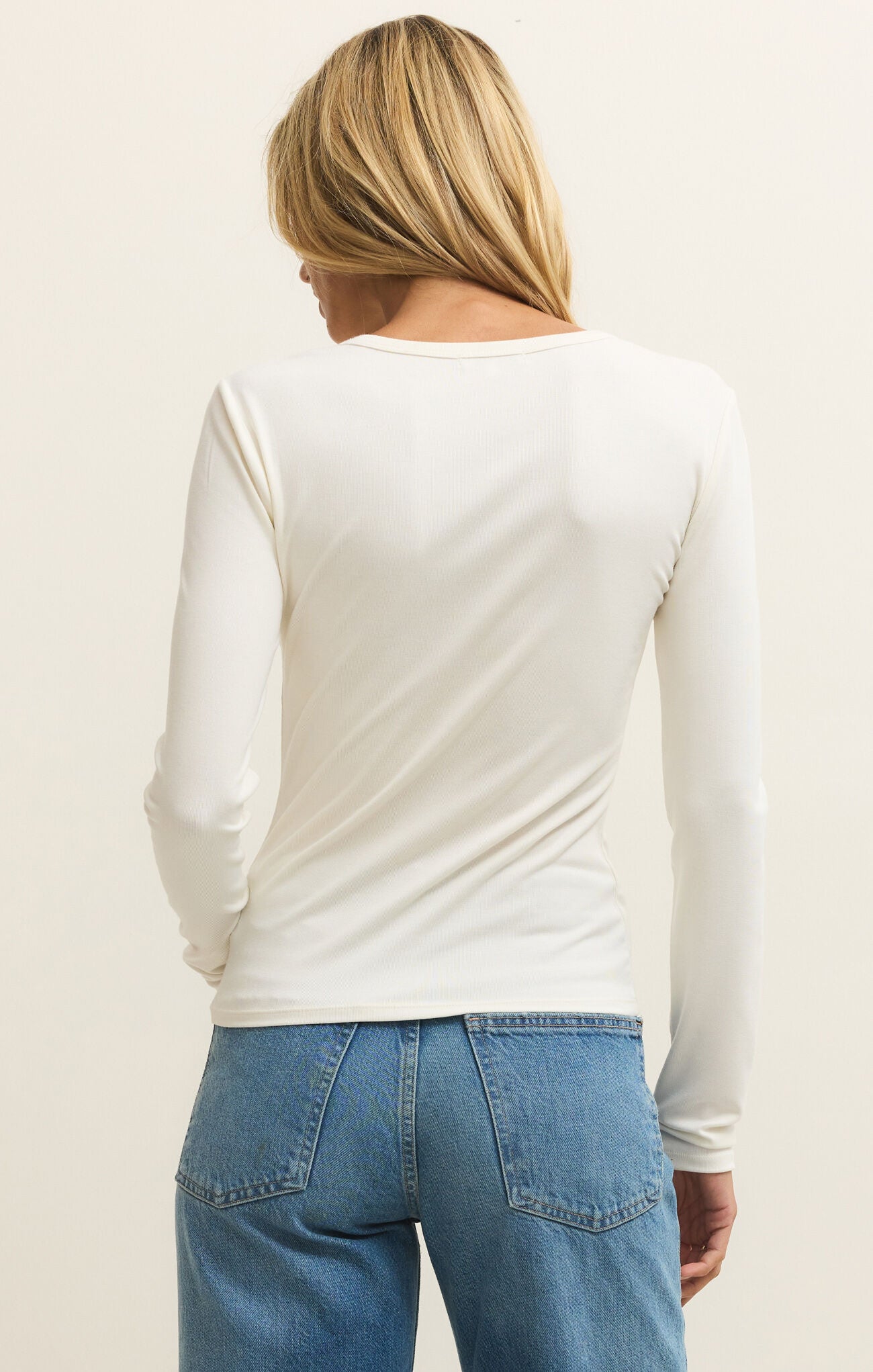 Person wearing a white long-sleeve top and blue jeans on a plain background