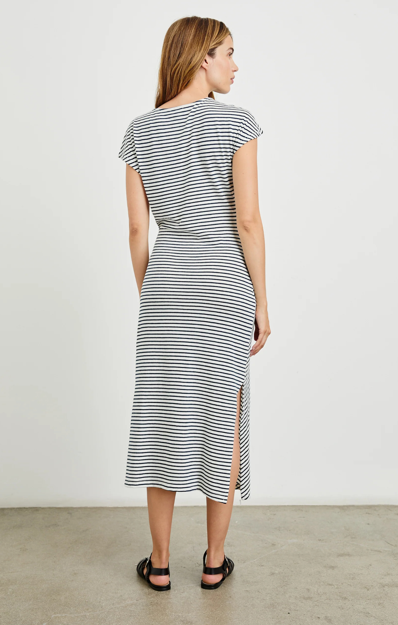 Woman wearing a black and white striped dress with a side slit against a plain background