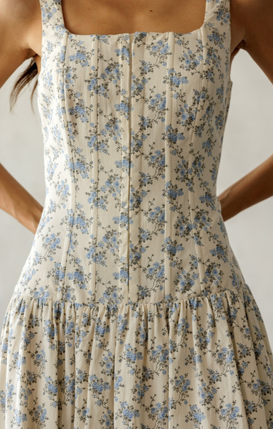 Beige dress with blue floral pattern worn by a person against a neutral background