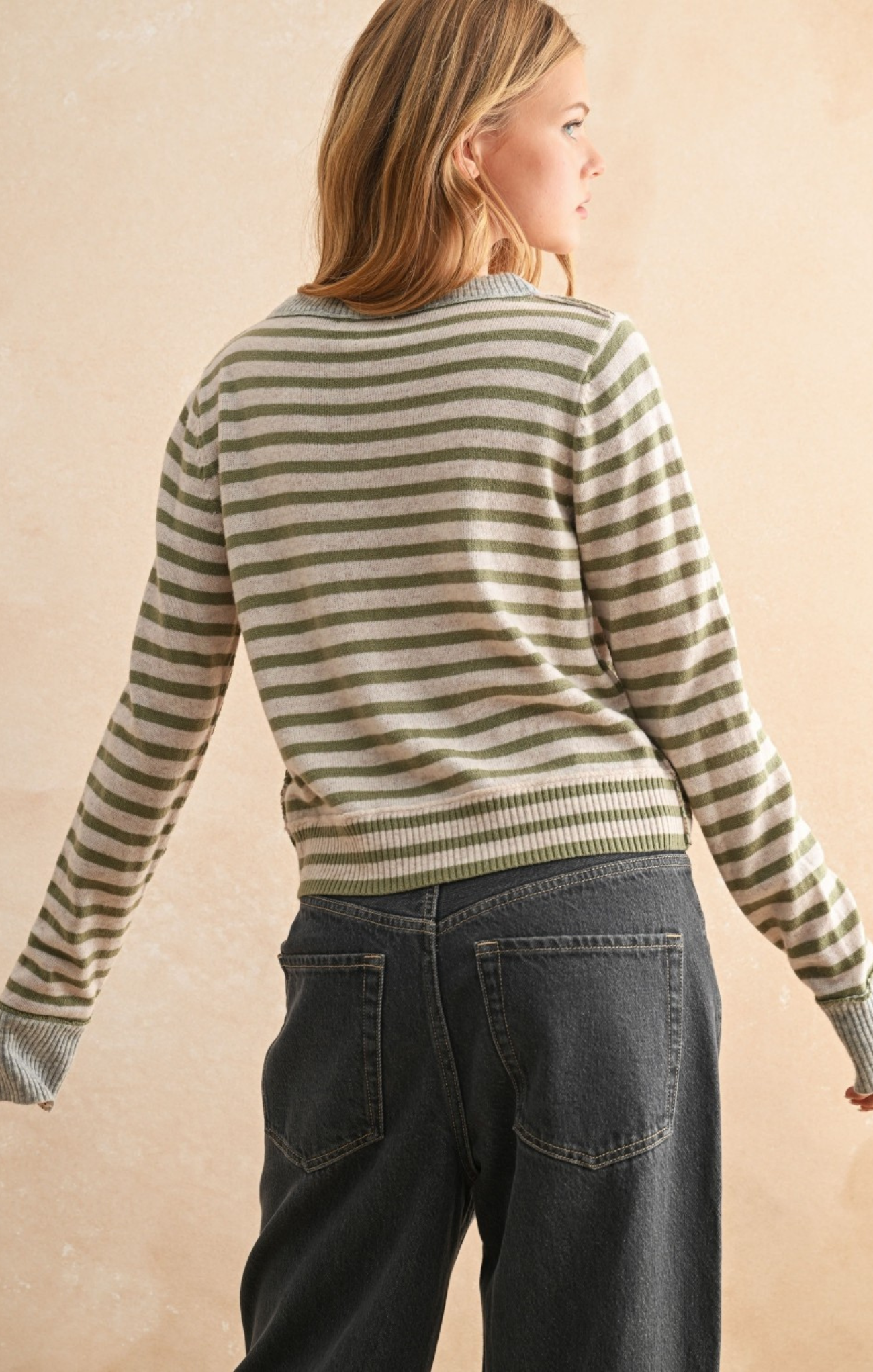 Person wearing a striped sweater and jeans against a beige background