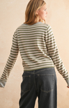 Person wearing a striped sweater and jeans against a beige background